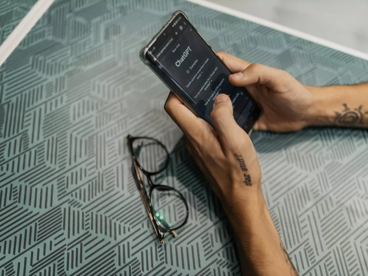 A person's hands holding a Realme GT 6 smartphone with a display showing the Magic Compose AI feature. The phone is on a patterned surface with a pair of eyeglasses nearby.